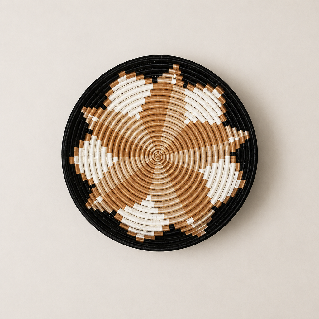 A round woven basket or tray with a geometric pattern in black, tan, and off-white, photographed from directly above on a light beige background.