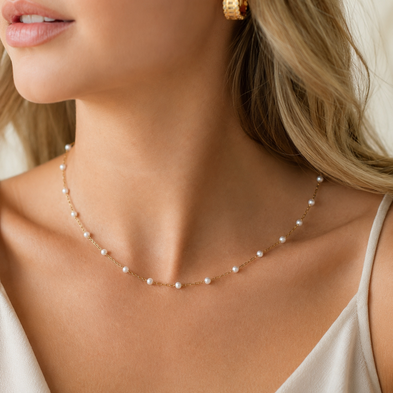 A delicate gold chain necklace with small white pearls spaced evenly along the front, worn by a model in a close-up shot.