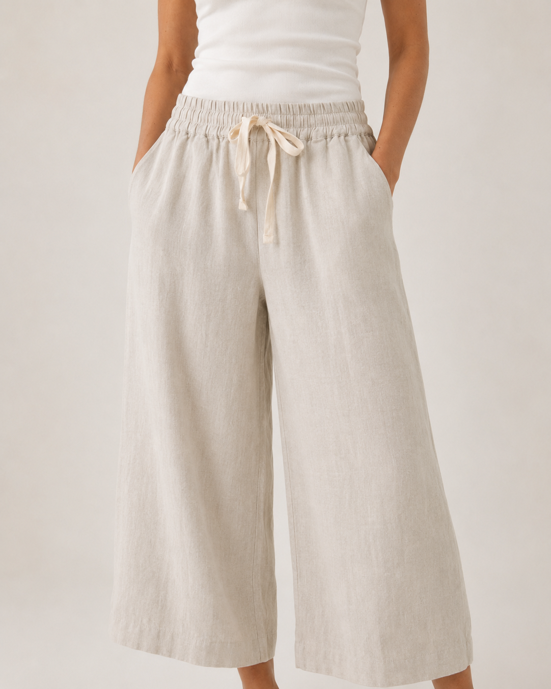 A person wearing loose, wide-leg cropped pants in a light warm neutral tone with an elastic drawstring waist, paired with a white top against a plain light background.