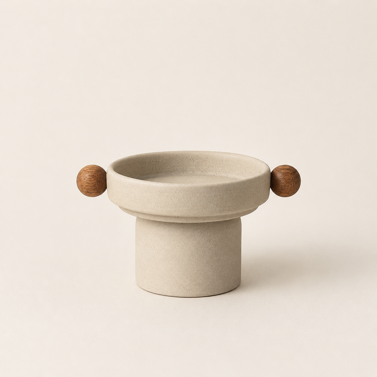 A minimalist ceramic bowl with a cylindrical pedestal base and two small wooden sphere handles on either side, shown on a warm off-white background.