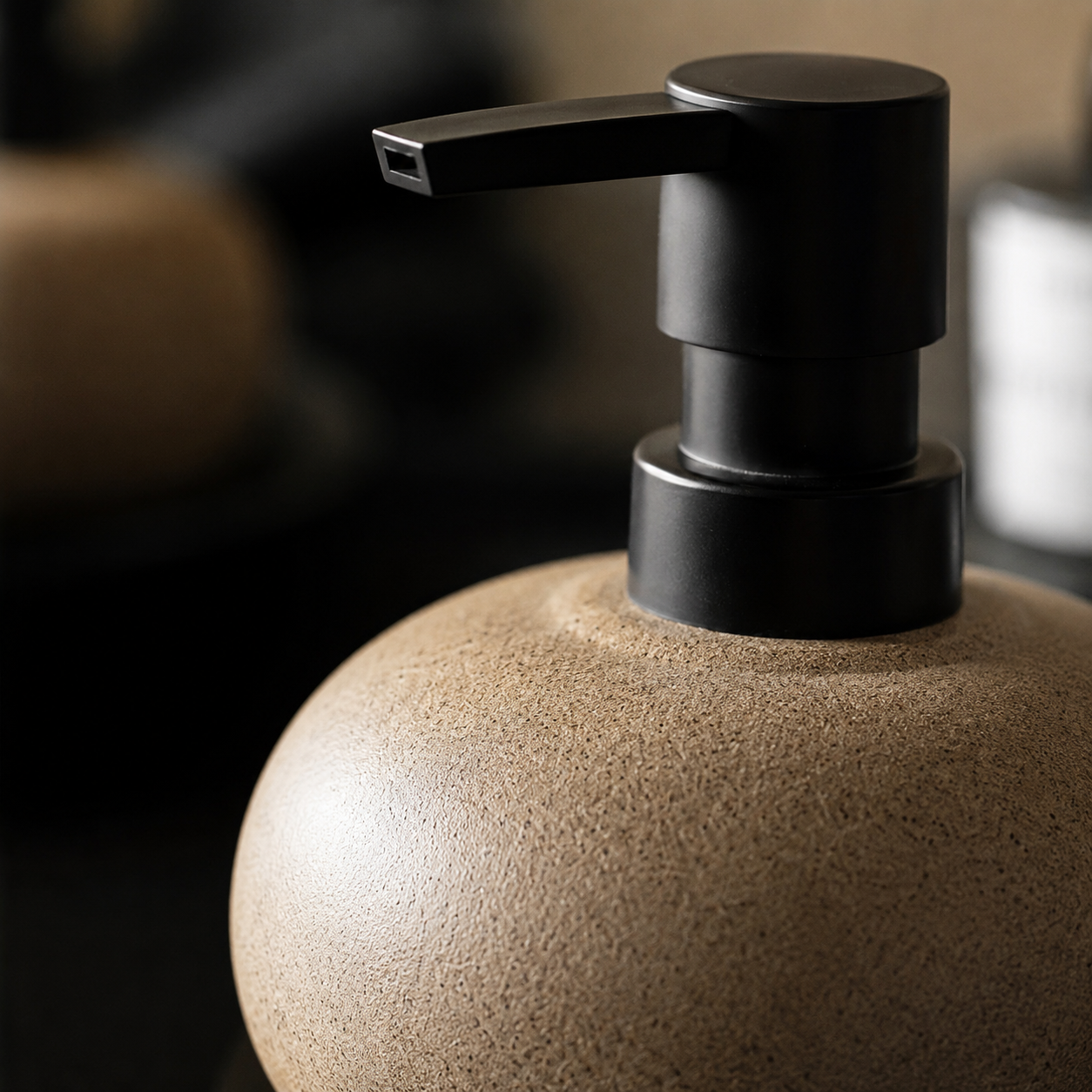 Close-up of a matte black pump dispenser mounted on a round, textured beige container, photographed in a softly blurred indoor setting.