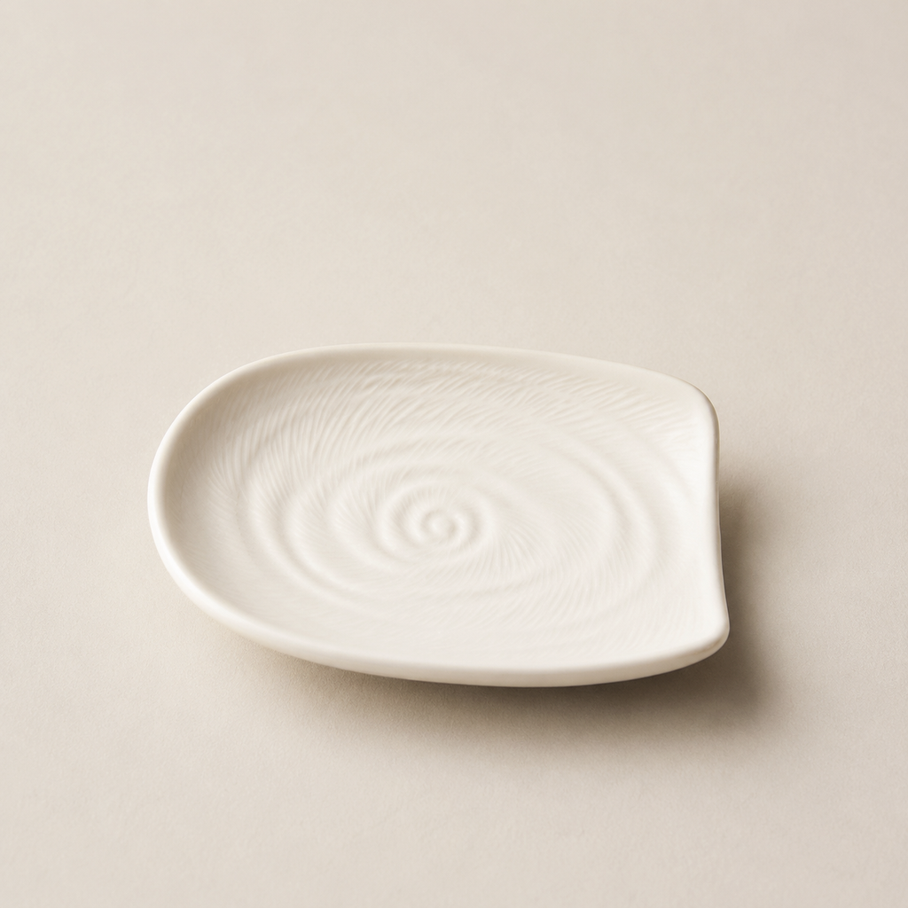 A small white ceramic plate with a textured spiral pattern on a light beige background.