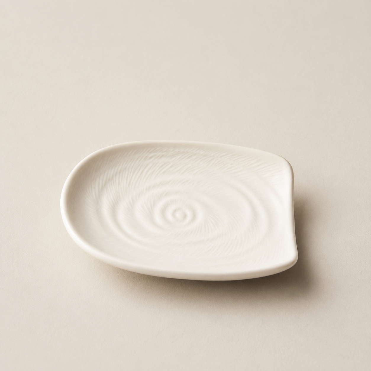A small white ceramic plate with a textured spiral pattern on a light beige background.