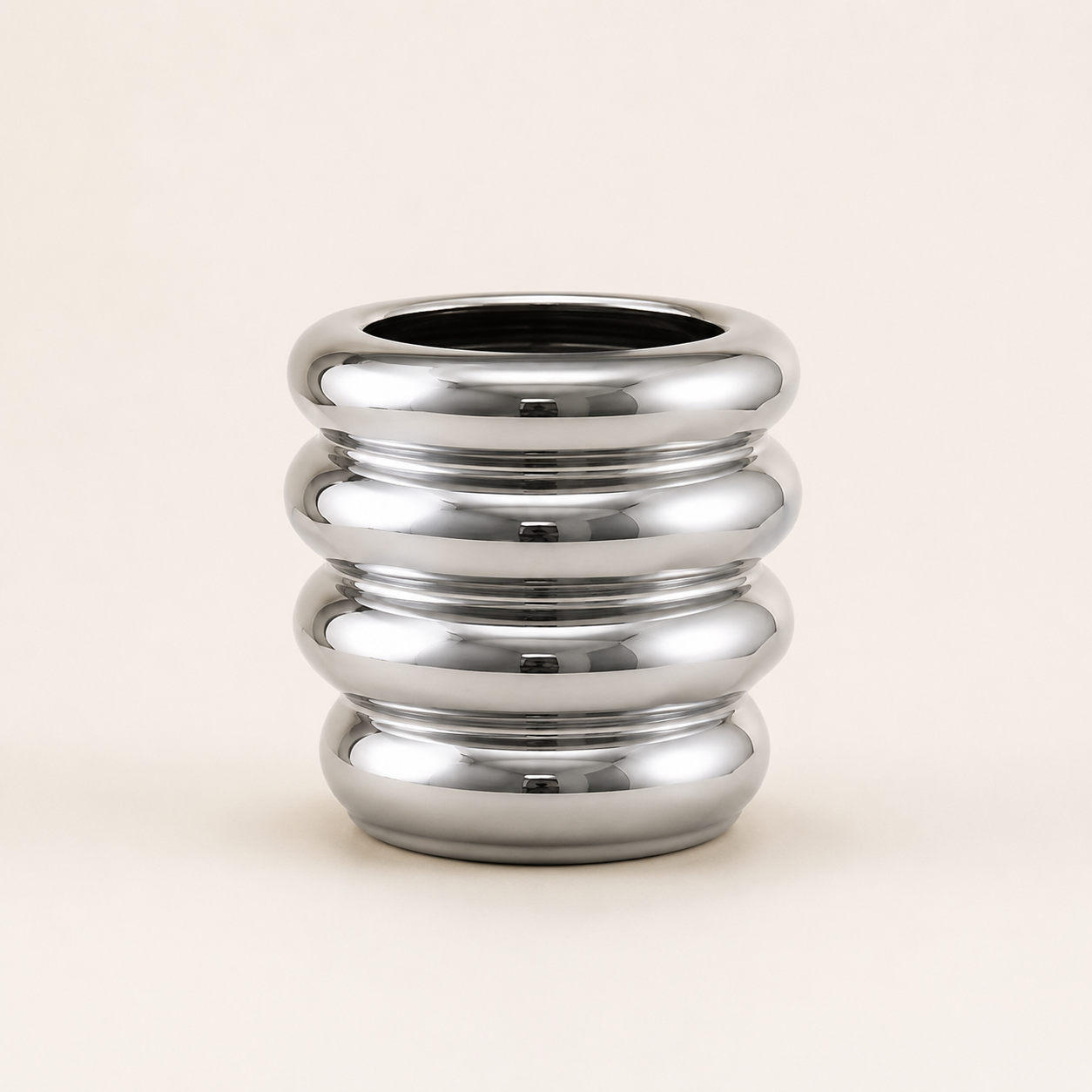 A polished chrome metallic vase with a ribbed, segmented cylindrical design, set against a solid light beige background.