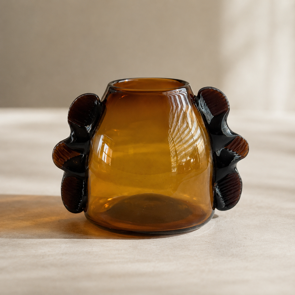 Amber glass vase with sculptural dark brown ram horns on the sides, set on a neutral beige surface with soft natural light.