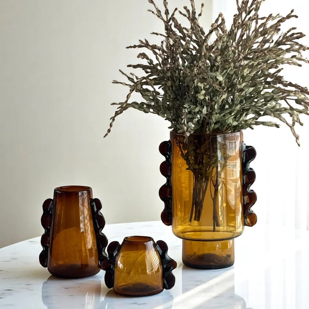 Set of three amber glass vases with decorative bases on a white surface.