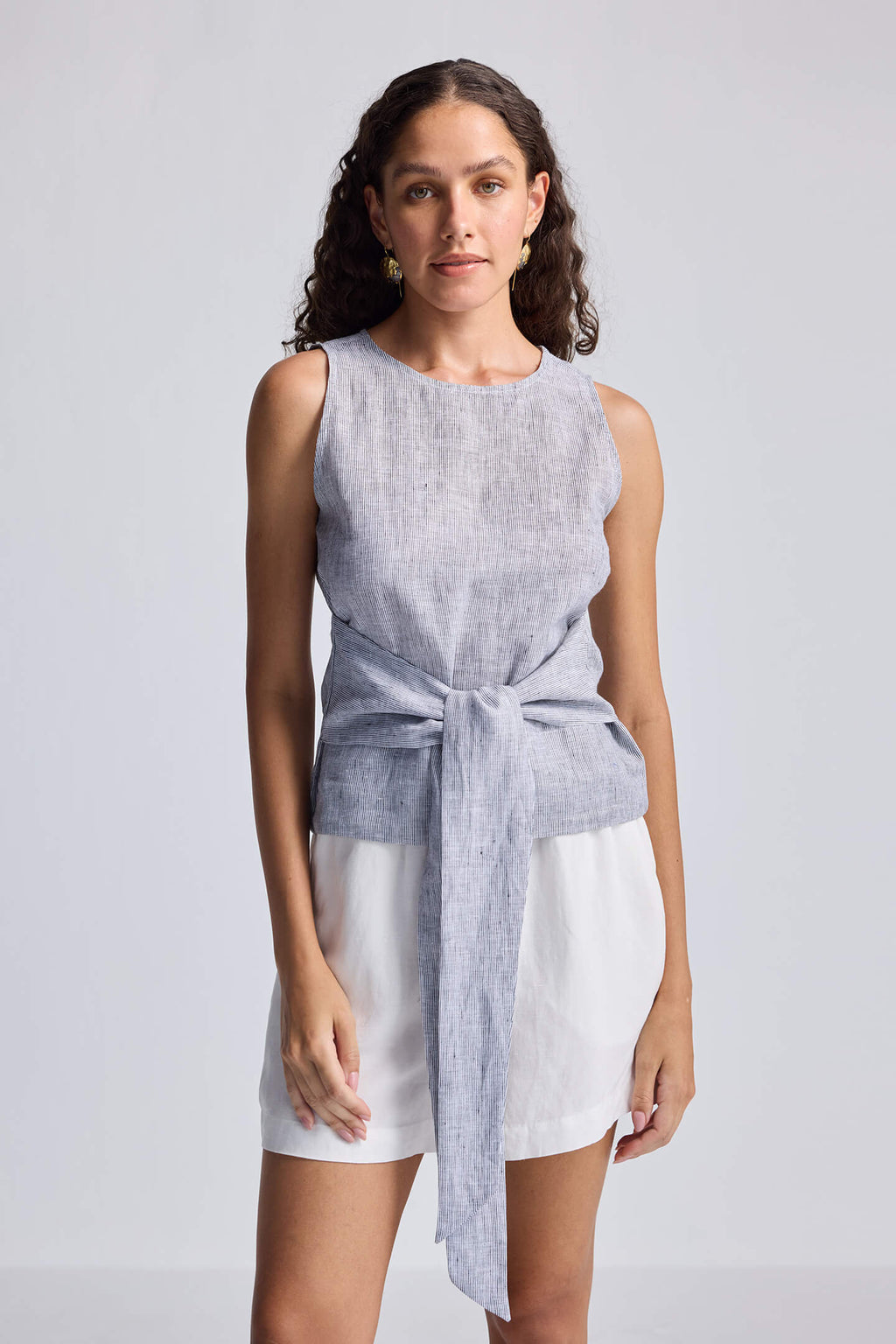 Woman wearing a sleeveless top and shorts with a tie detail on a plain background