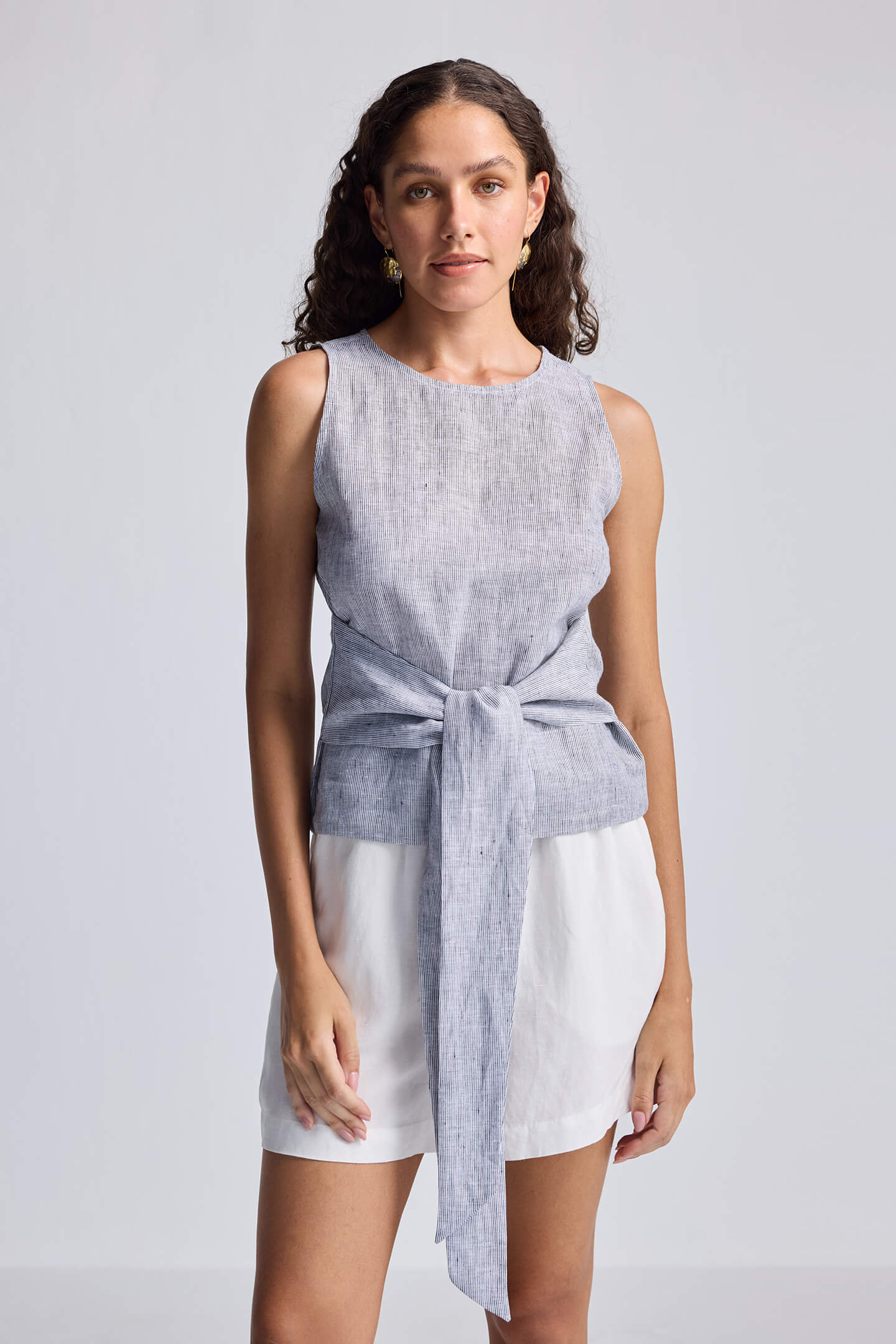 Woman wearing a sleeveless top and shorts with a tie detail on a plain background