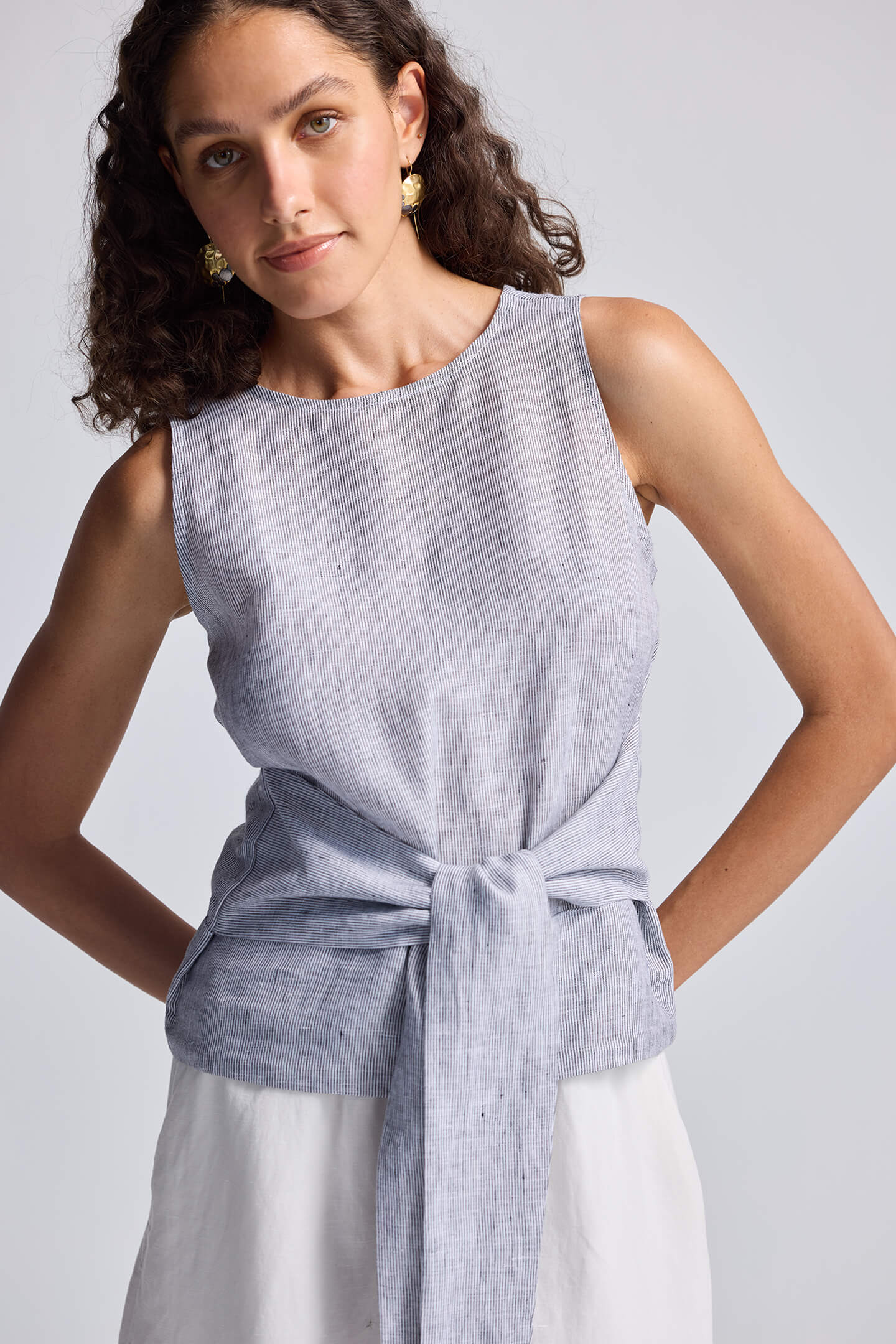 Woman wearing a sleeveless blue top with a tie detail on a light gray background