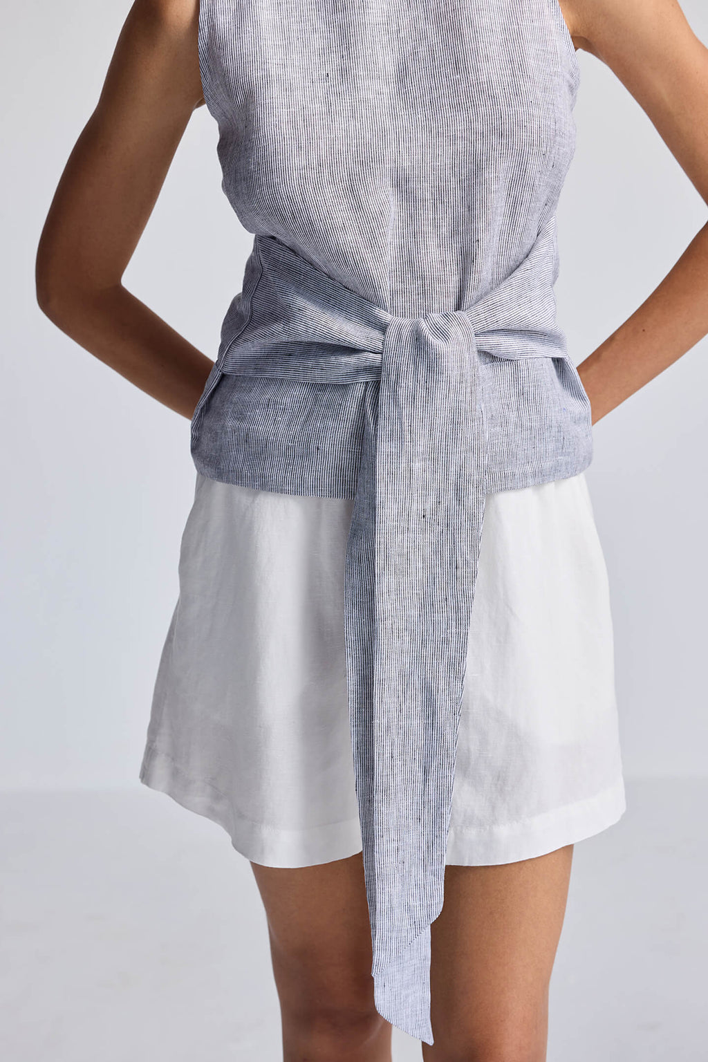 Person wearing a sleeveless gray top and white shorts with a gray belt on a light gray background