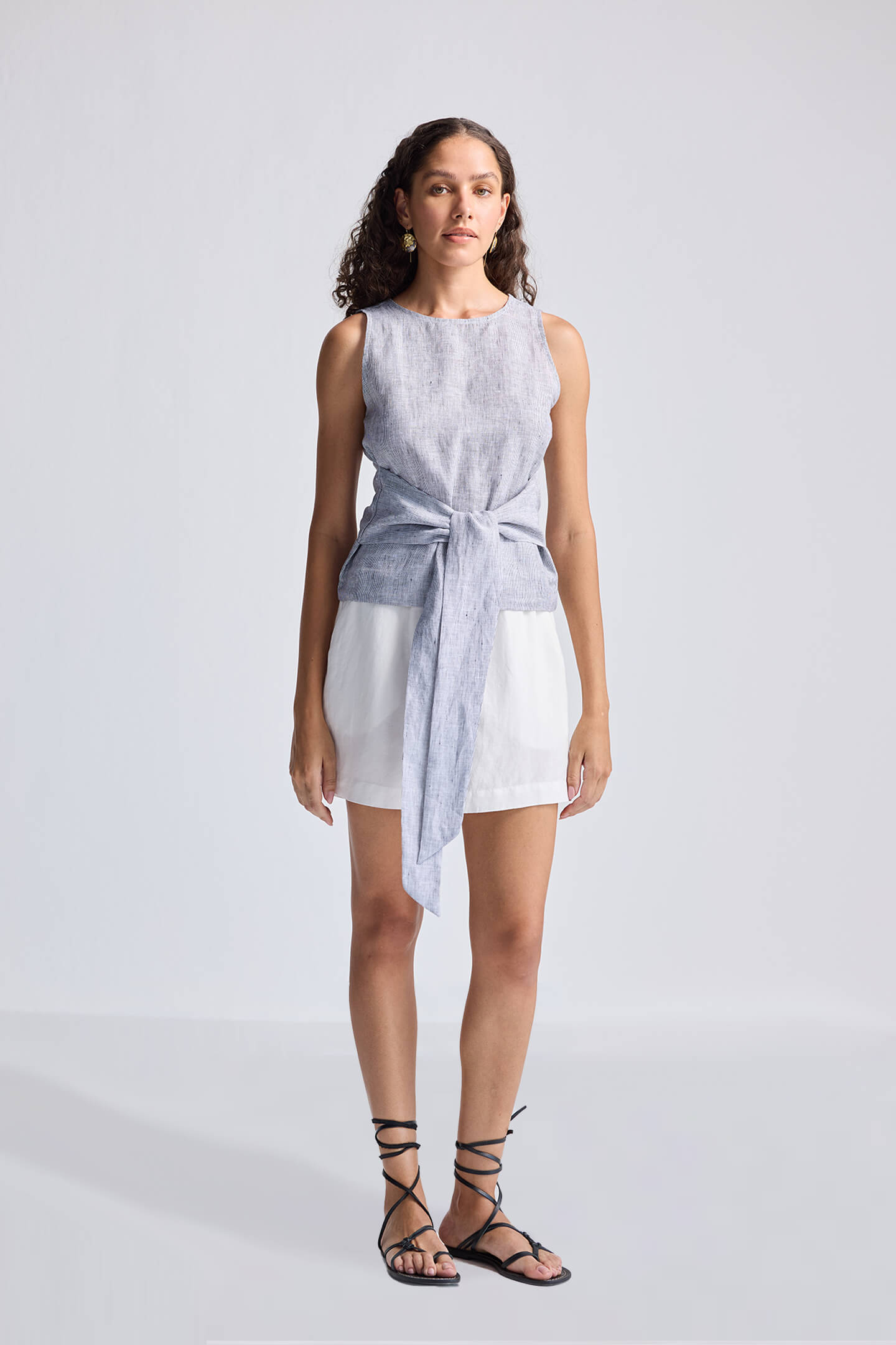 Woman wearing a sleeveless dress with a tie waist on a plain background