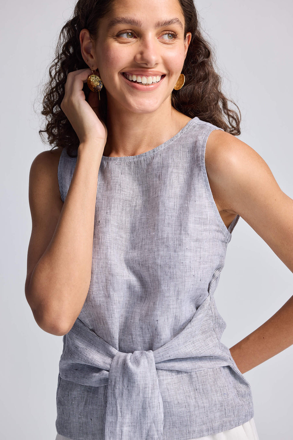 Woman wearing a light gray sleeveless top with a knot detail on a plain background
