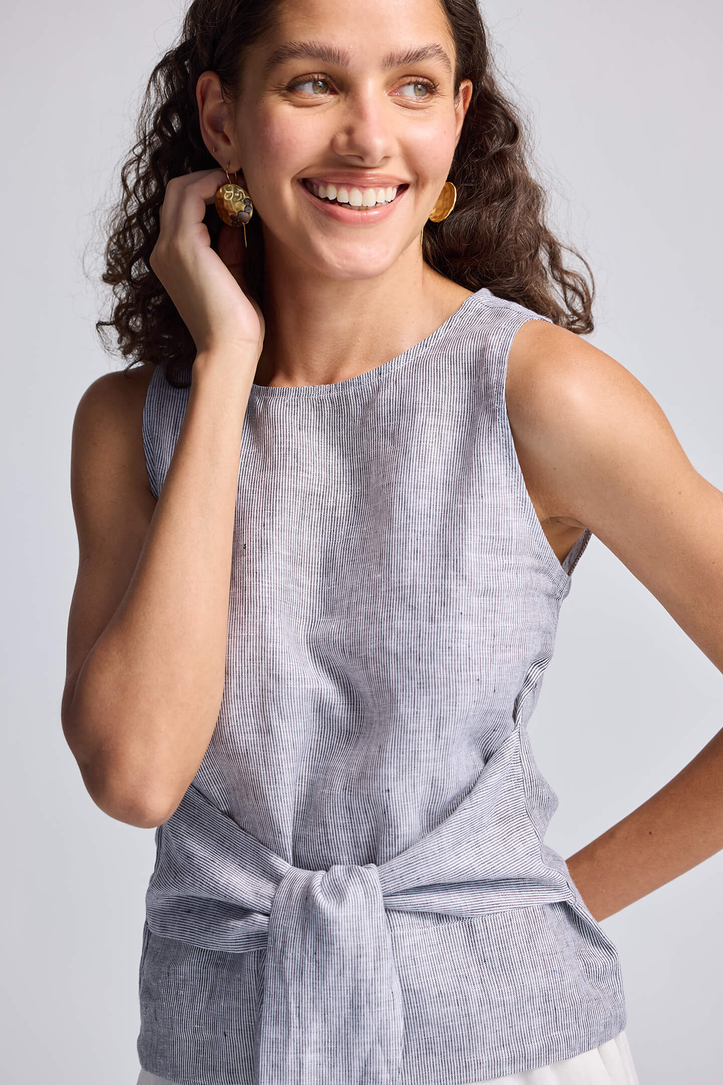 Woman wearing a light gray sleeveless top with a knot detail on a plain background