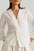 Woman wearing a white blouse with a knot detail on a plain background