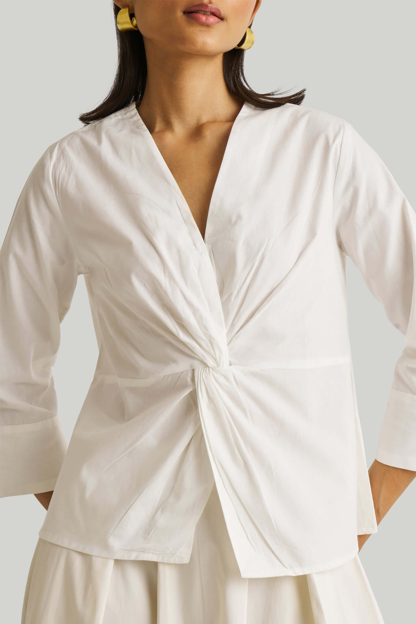 Woman wearing a white blouse with a knot detail on a plain background