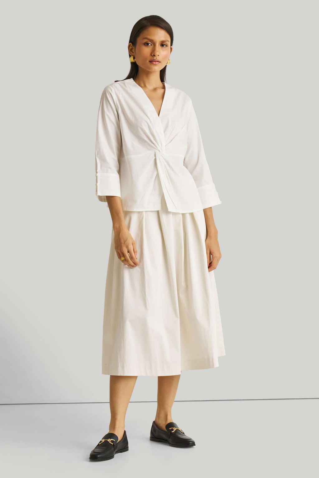 Woman wearing a white outfit with a top and skirt on a light gray background