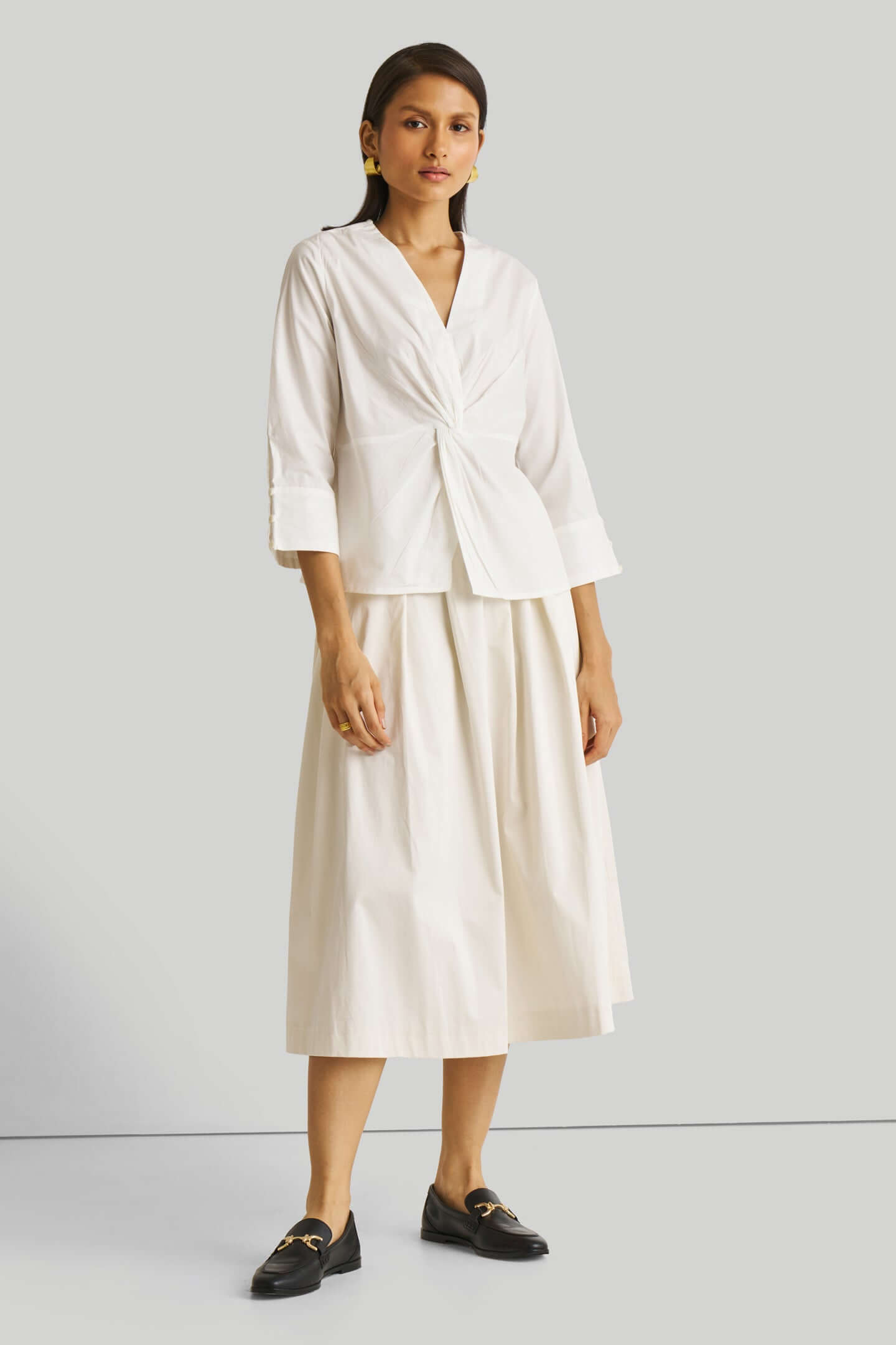 Woman wearing a white outfit with a top and skirt on a light gray background