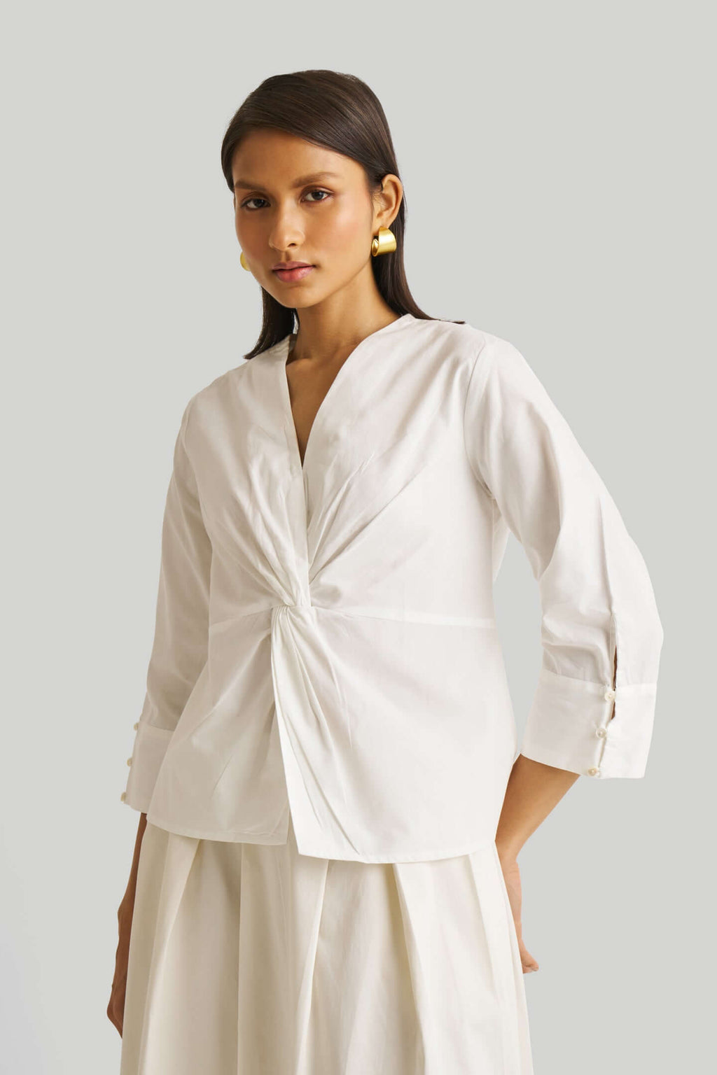 Woman wearing a white blouse with a knot detail on a plain background