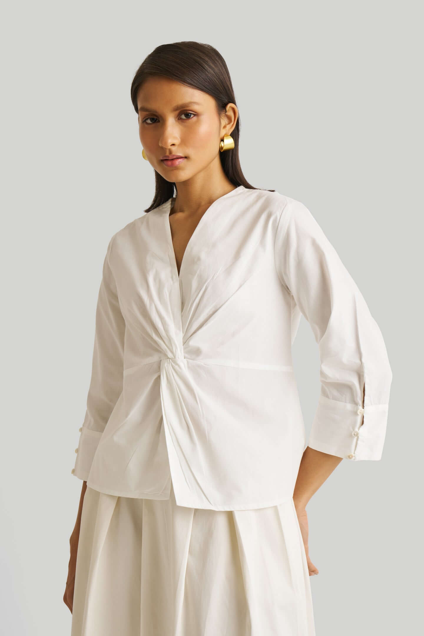 Woman wearing a white blouse with a knot detail on a plain background