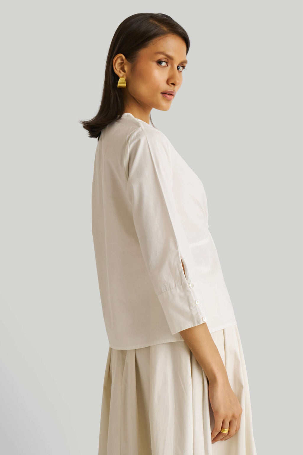 Woman wearing a white top and beige skirt on a light gray background