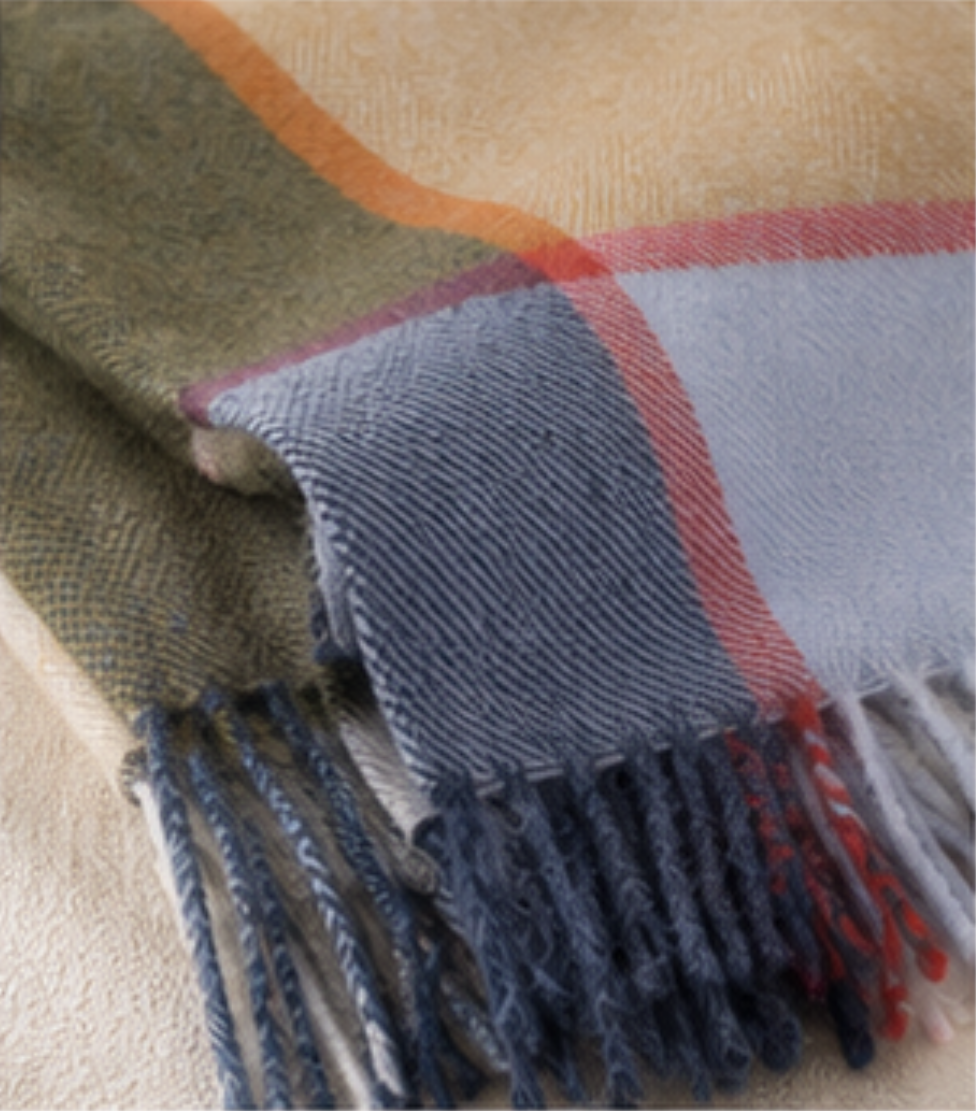 A close-up of a woven scarf with fringe, featuring a plaid pattern in olive green, light blue, gray, red, and cream.