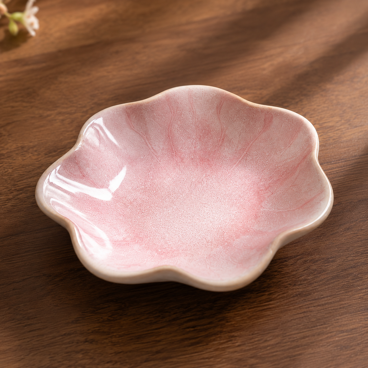 A small flower-shaped ceramic dish with a glossy pink interior and a warm off-white exterior, placed on a dark wooden surface.