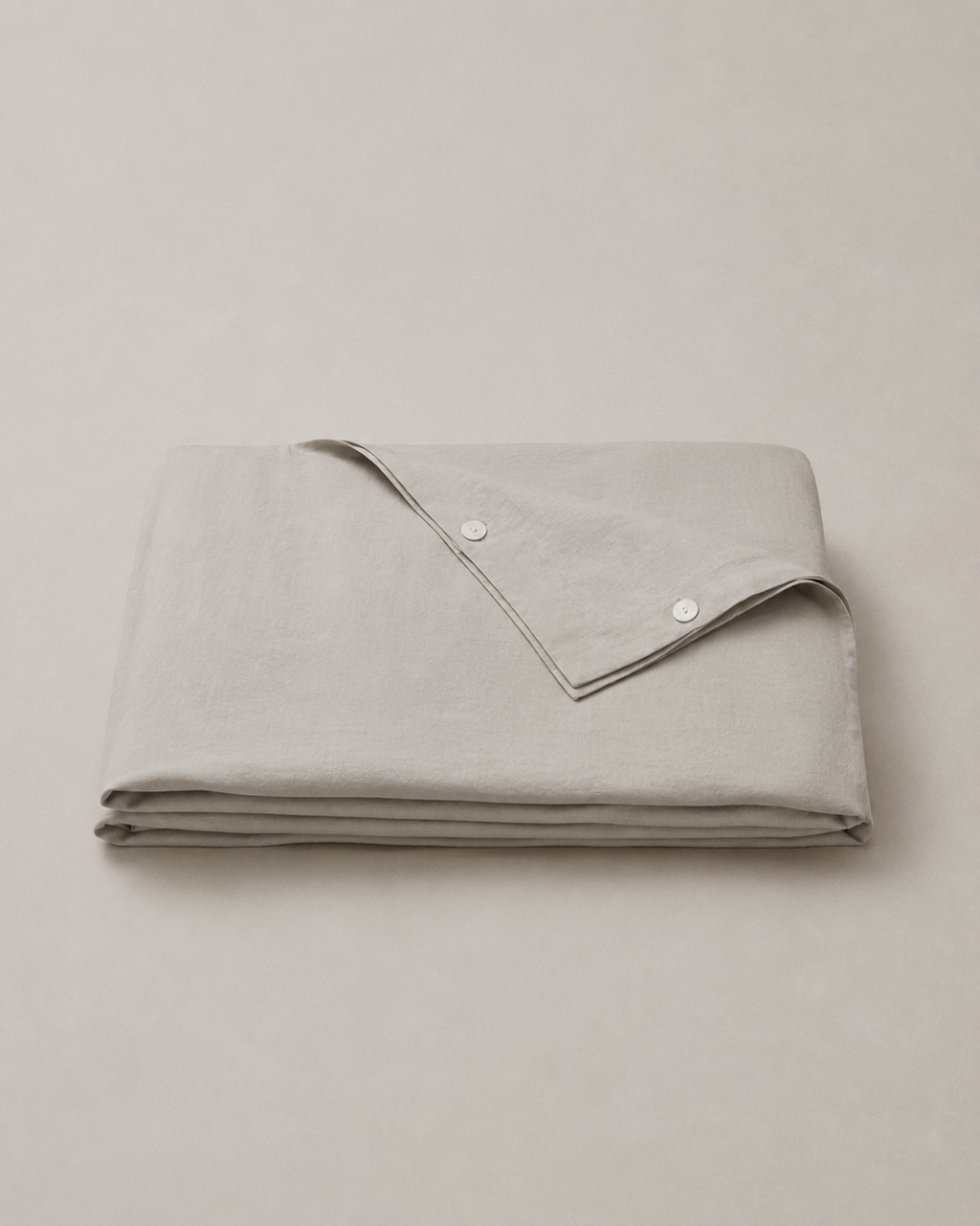 A folded light gray linen tablecloth with a matching folded napkin featuring two white buttons, set against a neutral light gray background.