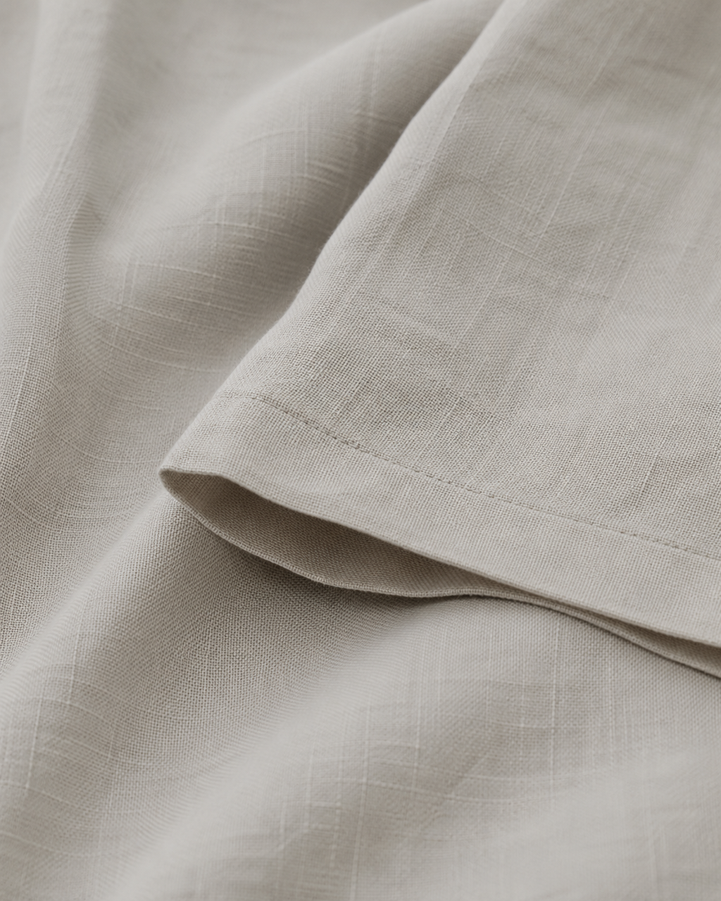 Close-up of a light beige fabric with a subtle crinkled texture and a folded hem detail.