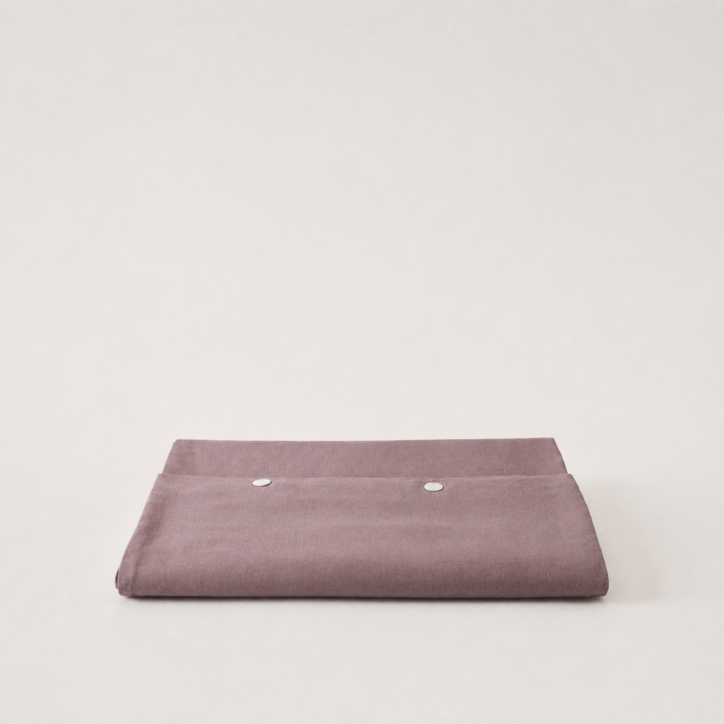A folded dusty purple fabric pouch or sleeve with two silver snap buttons, displayed on a clean, light off-white background.