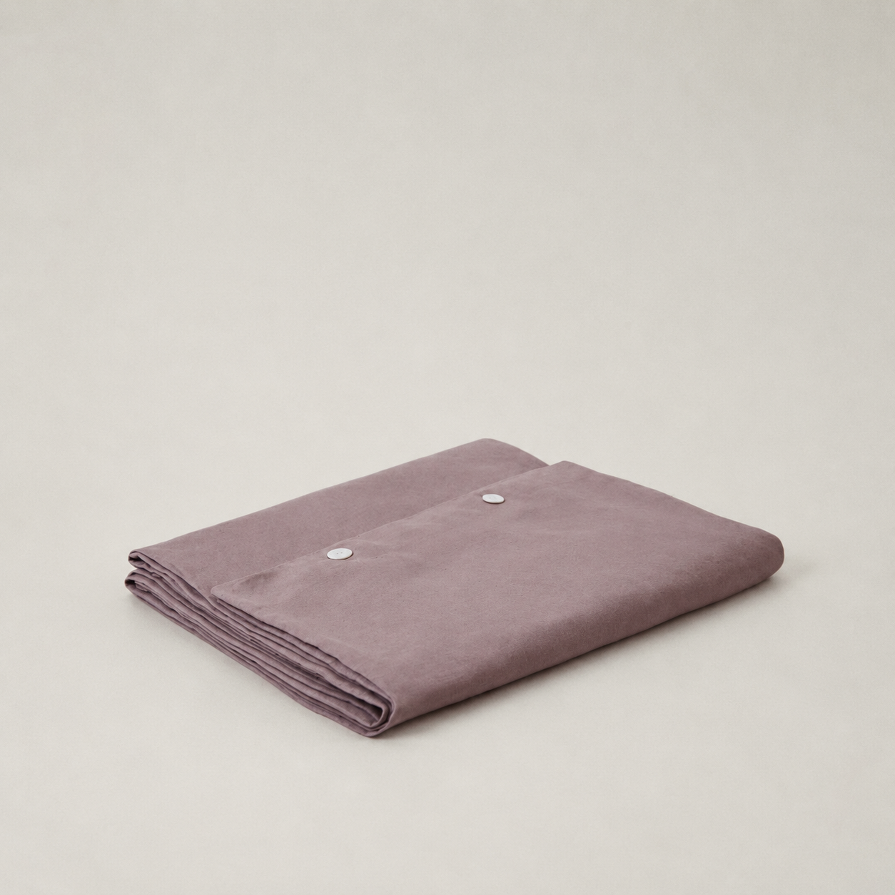 A folded dusty purple fabric item, likely a blanket or throw, featuring two silver snap buttons on the top edge, set against a plain light gray background.