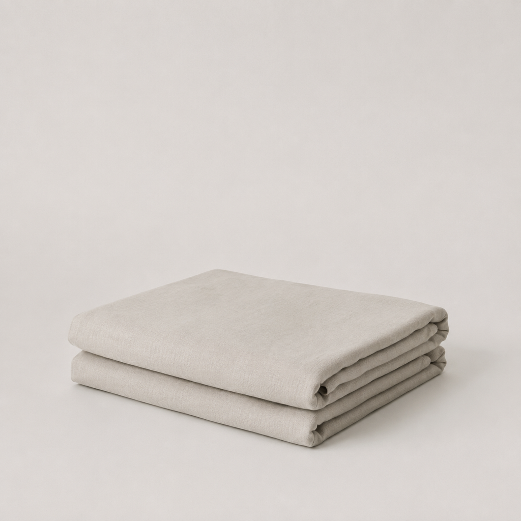 A folded light beige fabric item, likely a blanket or throw, displayed on a neutral light gray background.