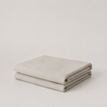 A folded light beige fabric item, likely a blanket or throw, displayed on a neutral light gray background.
