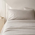 Light beige linen bedding set with a pillowcase on a bed in a softly lit neutral room.
