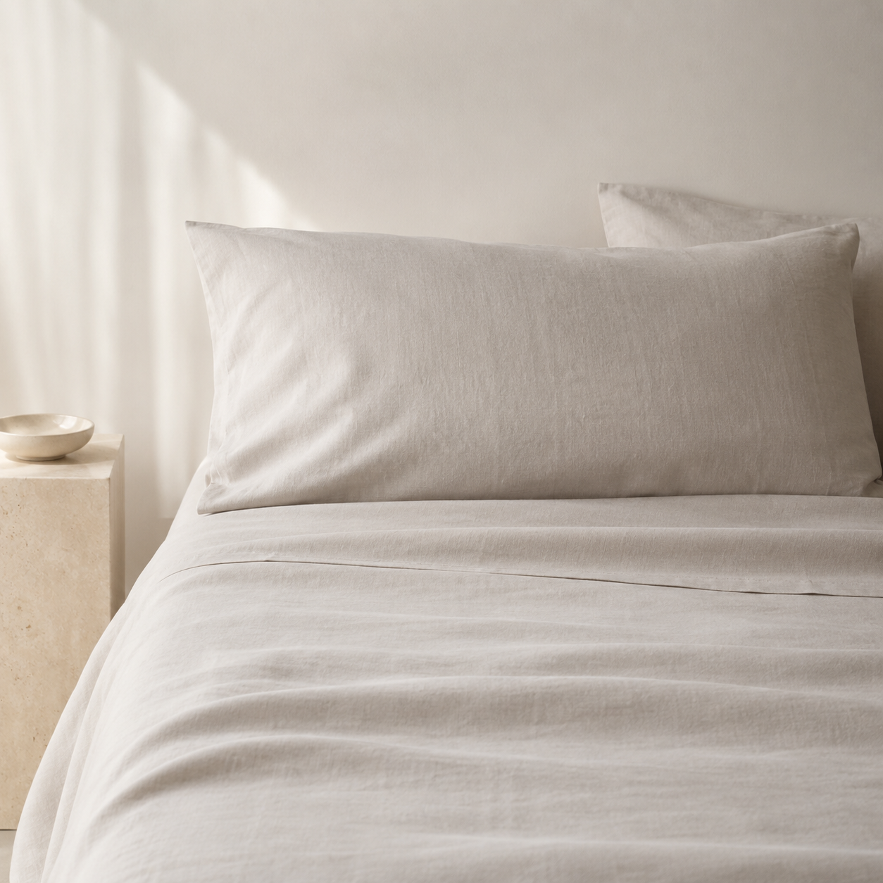Light beige linen bedding set with a pillowcase on a bed in a softly lit neutral room.