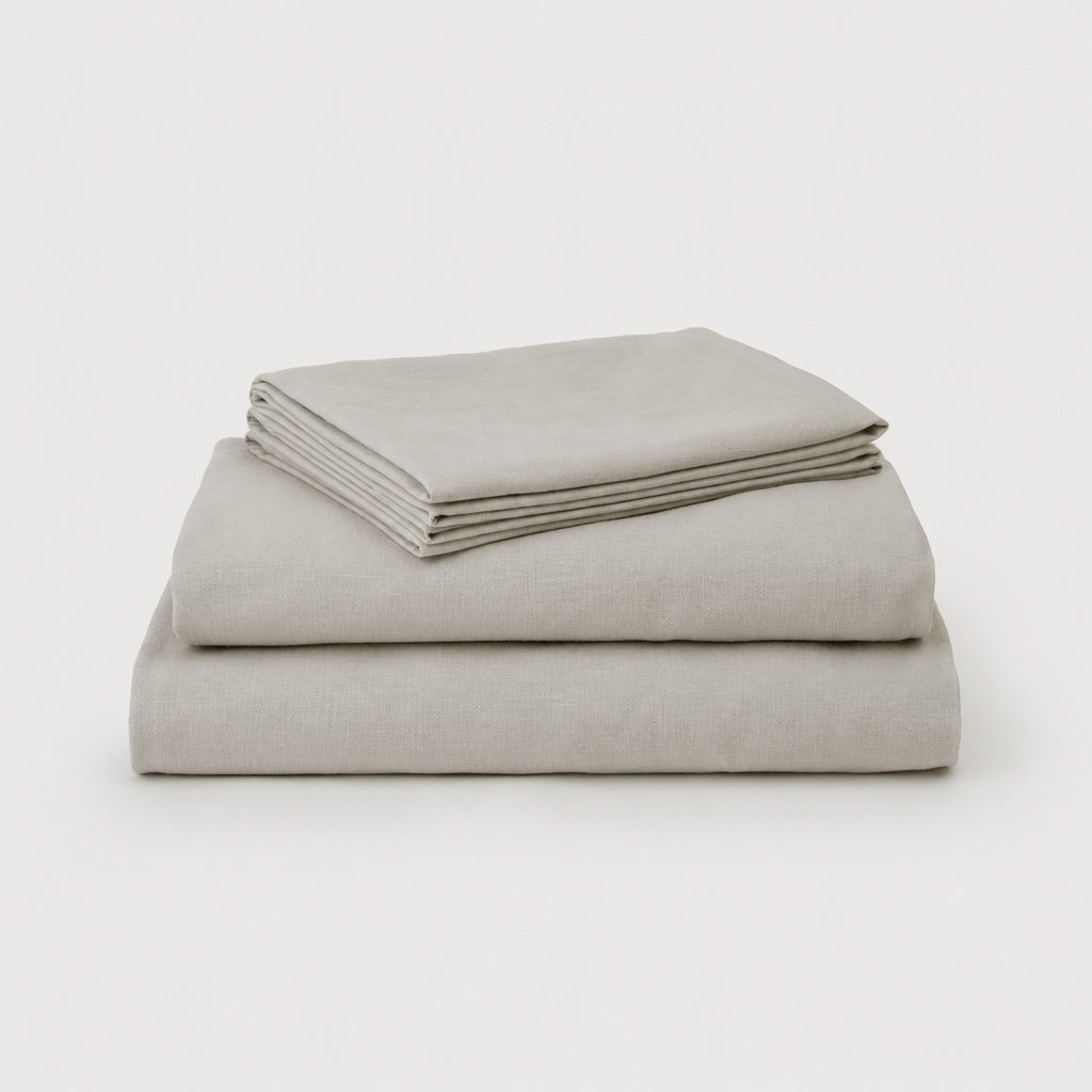 A stack of three neatly folded light gray linen sheets on a clean, light gray background.