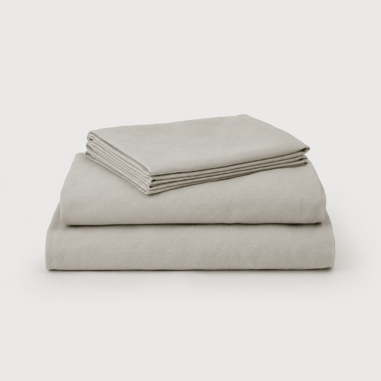 A stack of three neatly folded light gray linen sheets on a clean, light gray background.