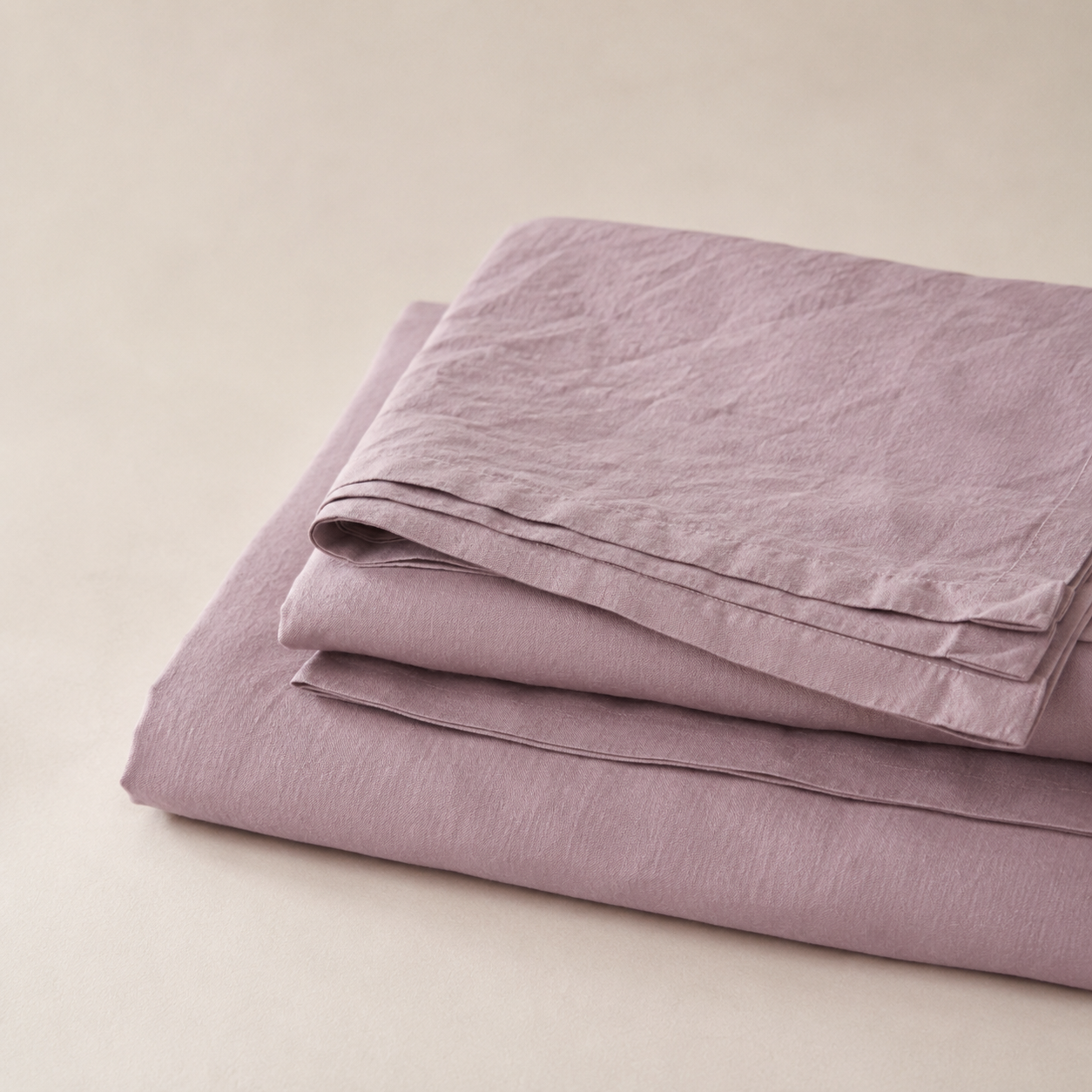 A folded dusty purple linen sheet set on a neutral beige background.