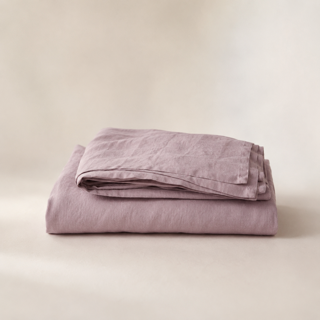 A folded dusty purple linen sheet or pillowcase set, displayed on a neutral beige background.