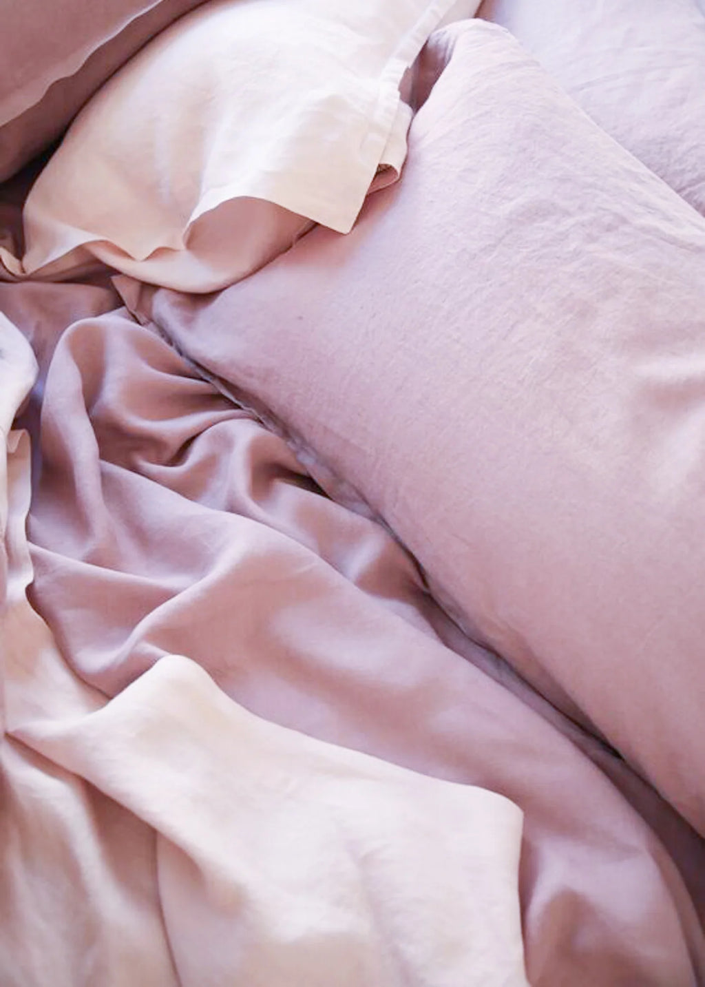 Close-up of soft blush pink bedding with a pillow and rumpled sheets, showing a delicate satin-like sheen.