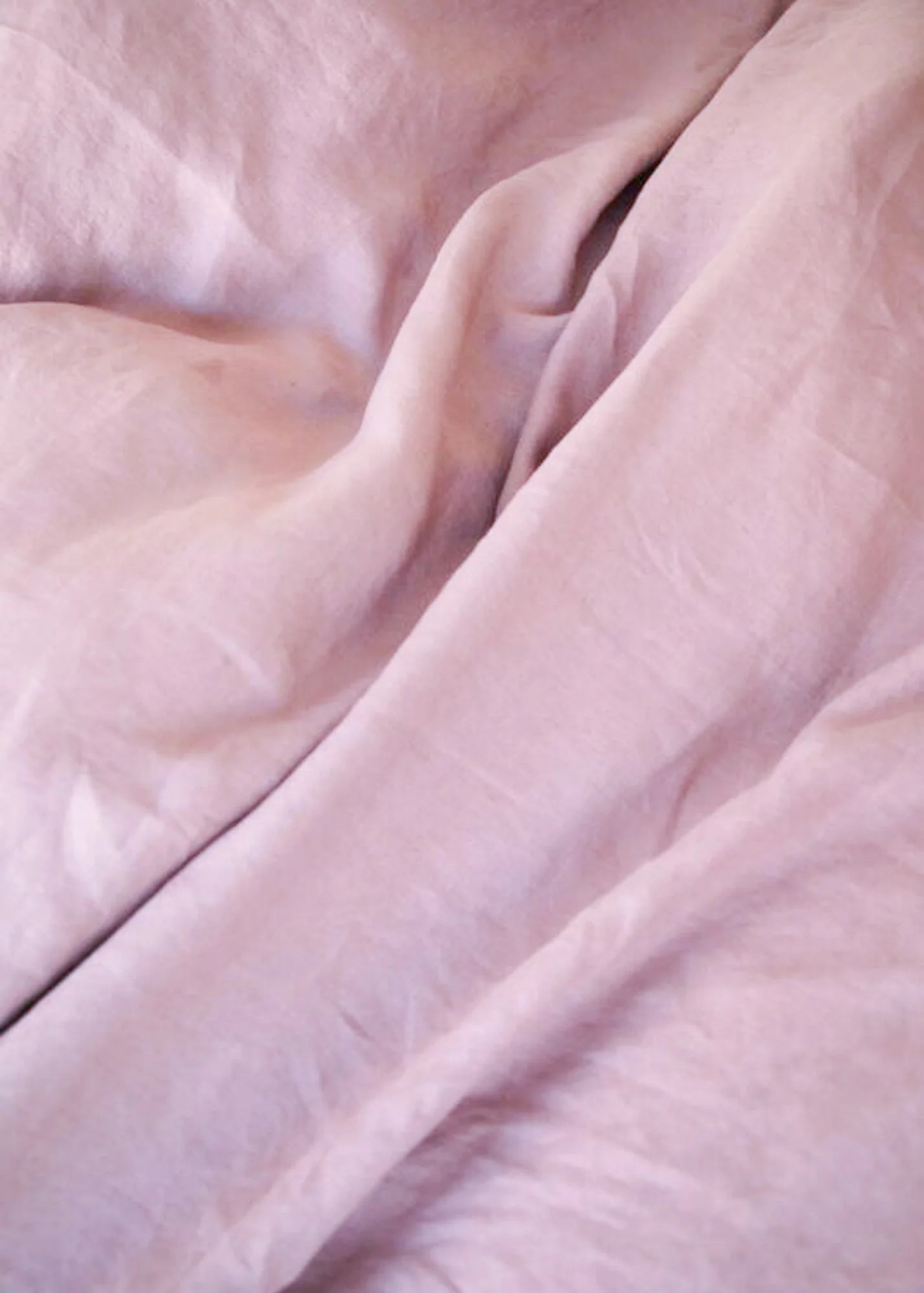 A close-up of draped dusty pink fabric with soft folds and a slightly textured surface.