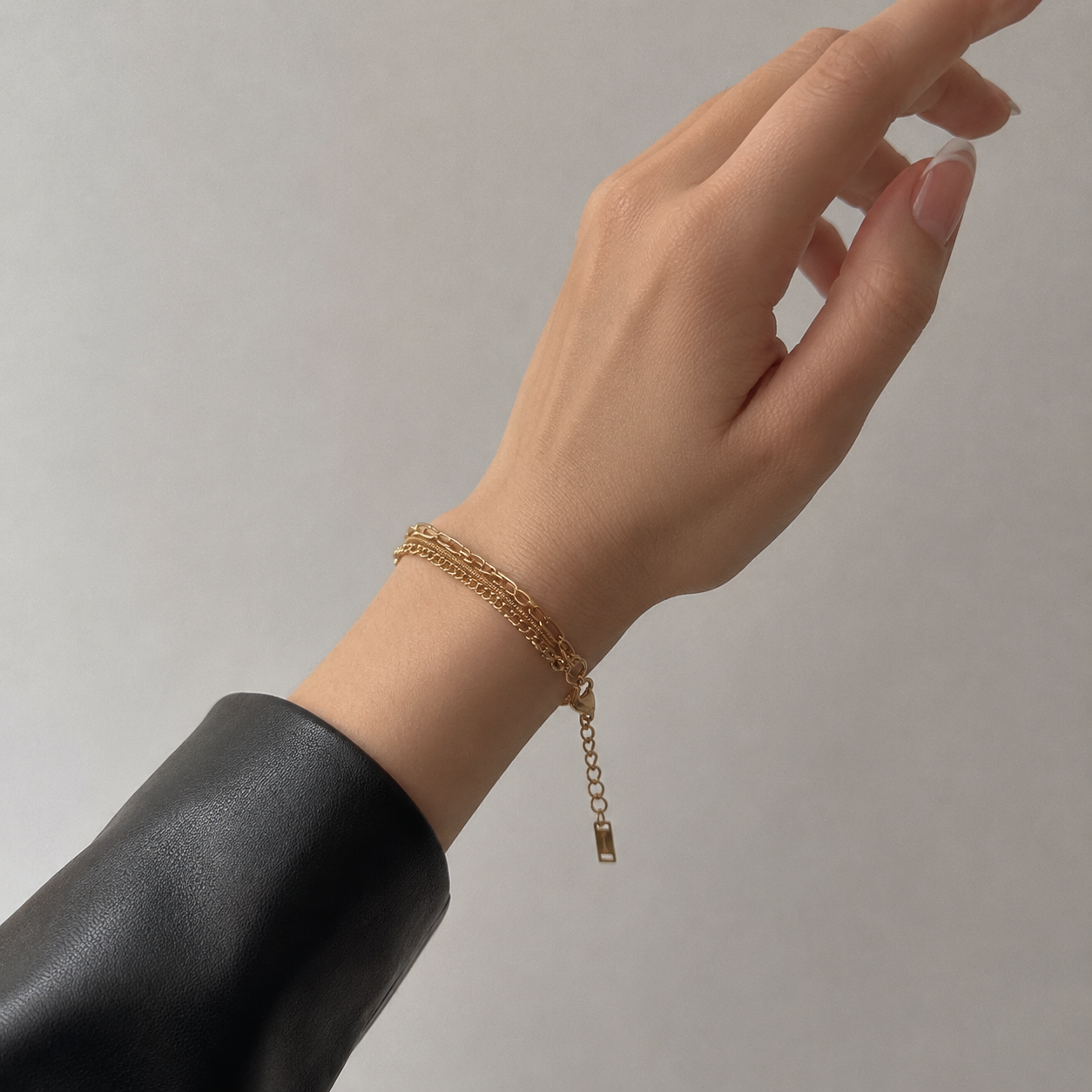 A delicate gold chain bracelet with an adjustable lobster clasp and small dangling tag, shown worn on a person's wrist against a plain light gray background.