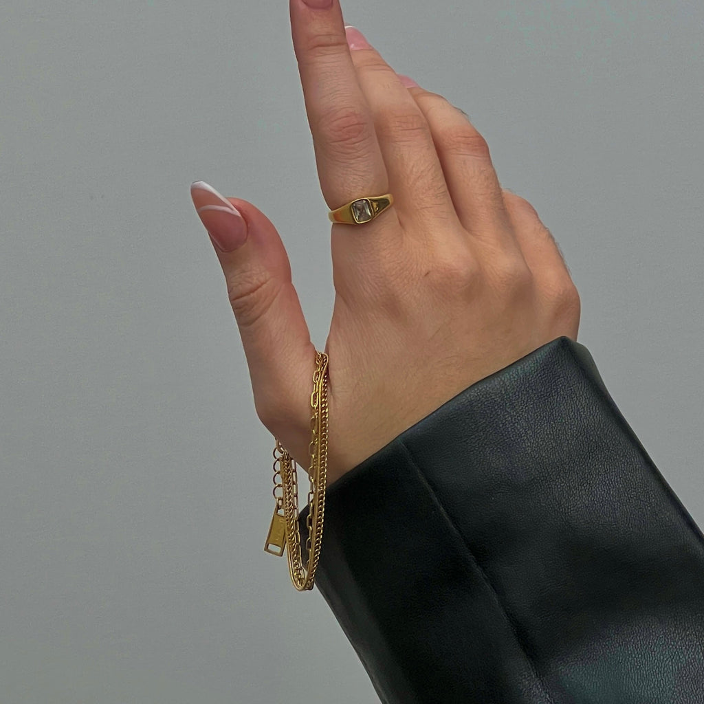Hand wearing gold rings and bracelets on a gray background