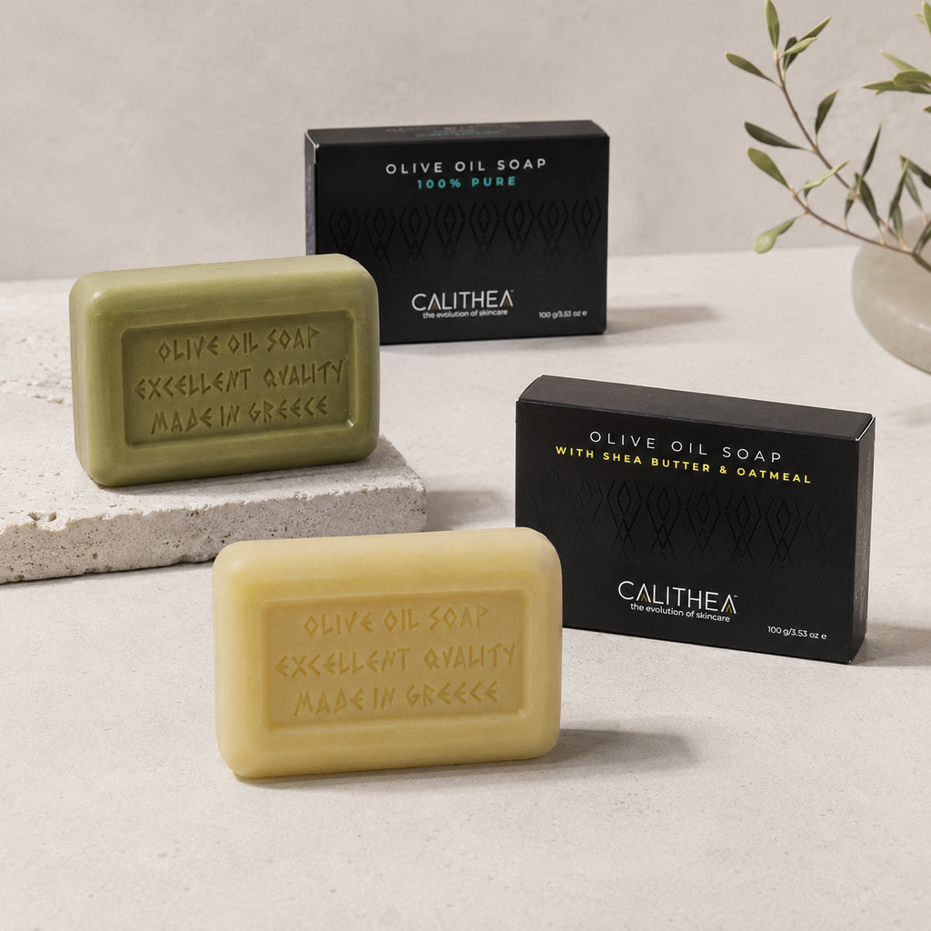 Three Calithea olive oil soap bars in different shades of green and yellow-beige are displayed alongside their black packaging boxes on a light stone surface.