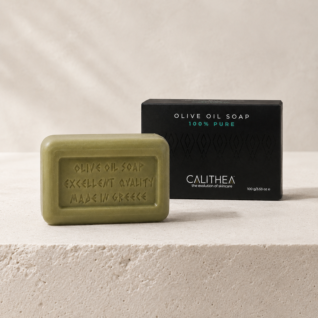 An olive green rectangular bar of Calithea olive oil soap sits in front of its black packaging box on a light beige textured stone surface.