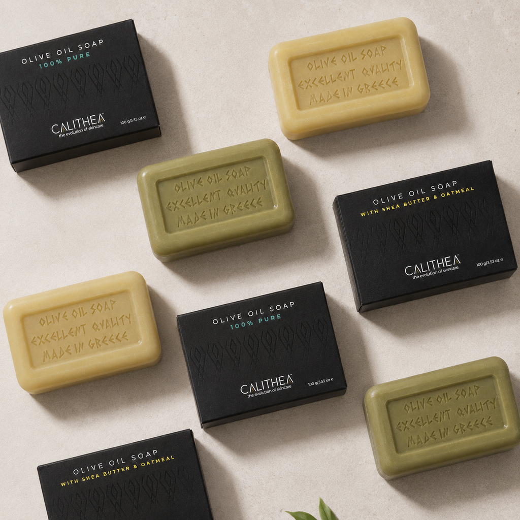 Six bars of Calithea Olive Oil Soap arranged on a light beige textured surface with their corresponding black packaging boxes. The soap bars alternate between a pale yellow-beige and an olive green color, and the boxes are black with white and gold text.