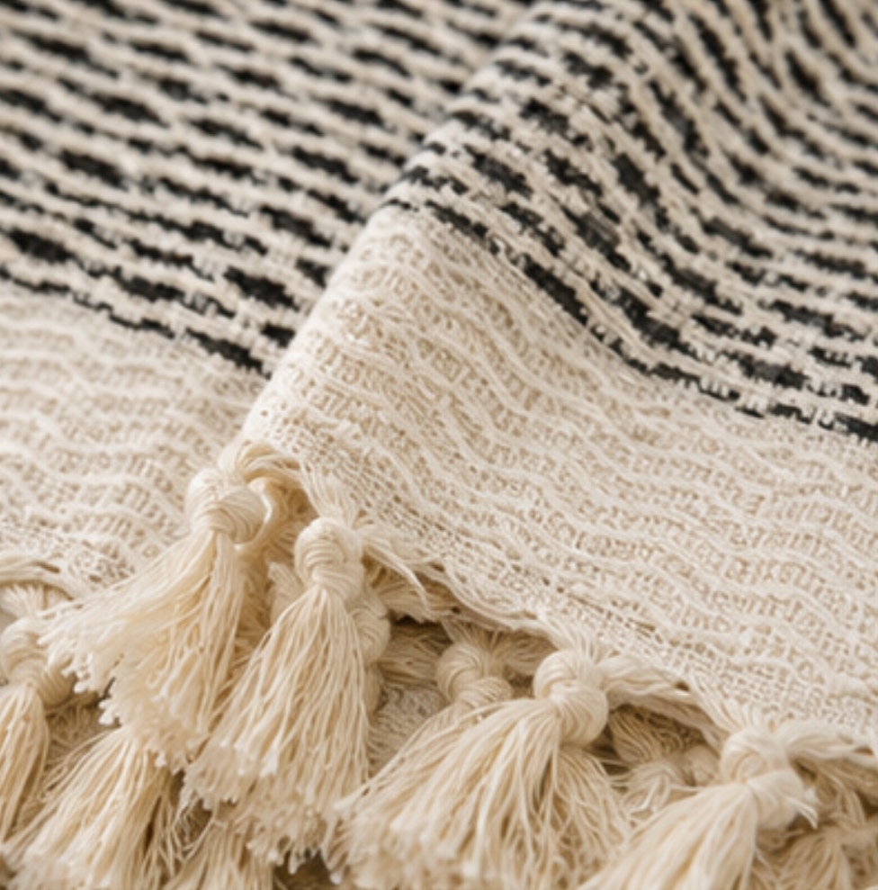 Close-up of a woven throw blanket with black and cream stripes and knotted fringe tassels.