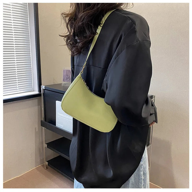 Person wearing a black outfit with a green shoulder bag indoors.