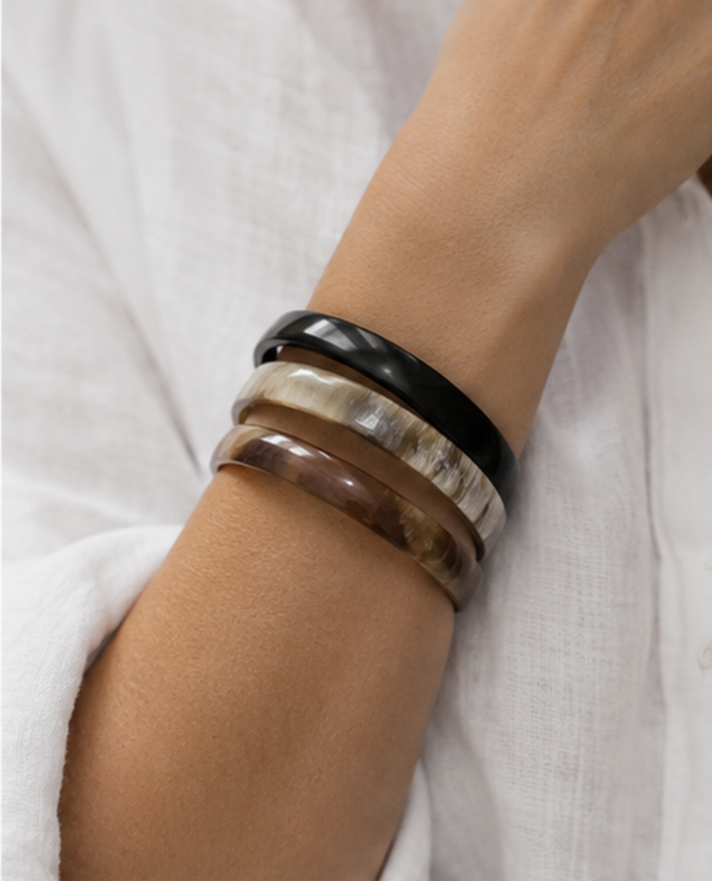 A close-up of a person's wrist wearing four stacked bangles: one black, one cream and brown marbled, one smoky brown, and one translucent brown.