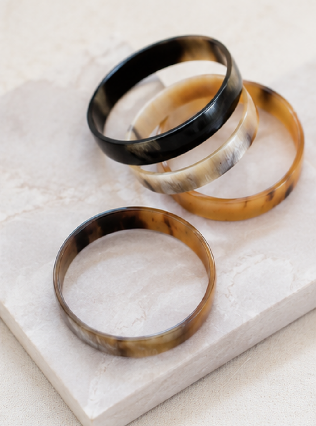 Three tortoiseshell bangles in black, cream, and brown tones, stacked on a light beige stone surface.