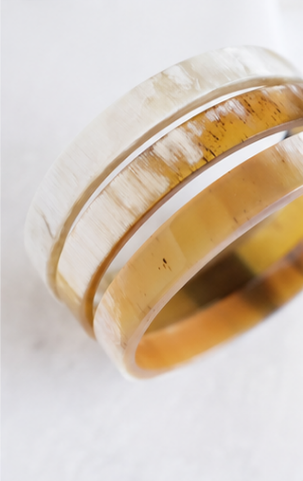 A close-up of a ring with a white inlay and a warm amber-brown outer band showing natural marbling and tiny dark inclusions, photographed on a light neutral background.